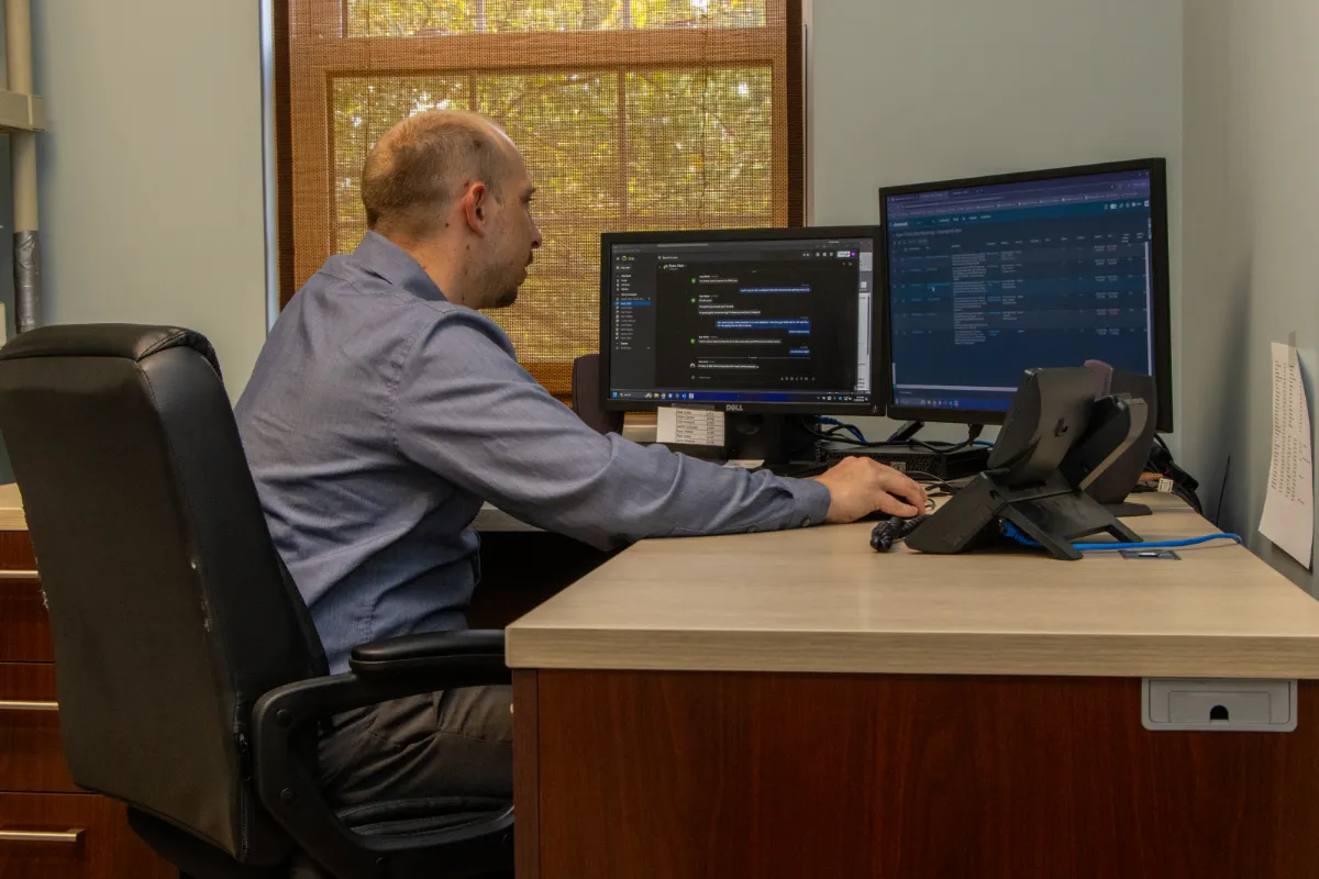 IT professional working at a desk with dual monitors in an office, managing systems and network operations